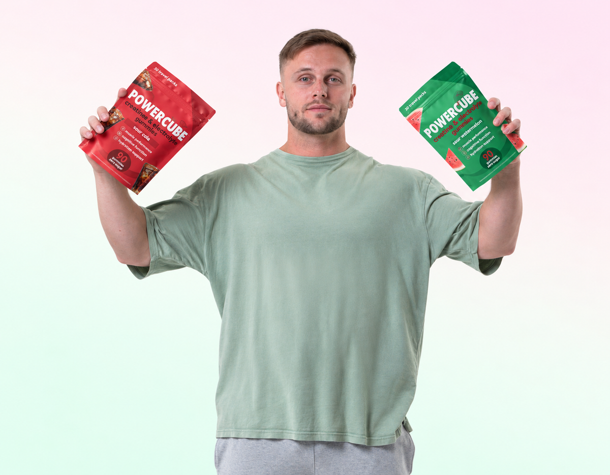 A man holding two pouches of POWERCUBE protein powder, one red and one green, against a soft pastel gradient background.