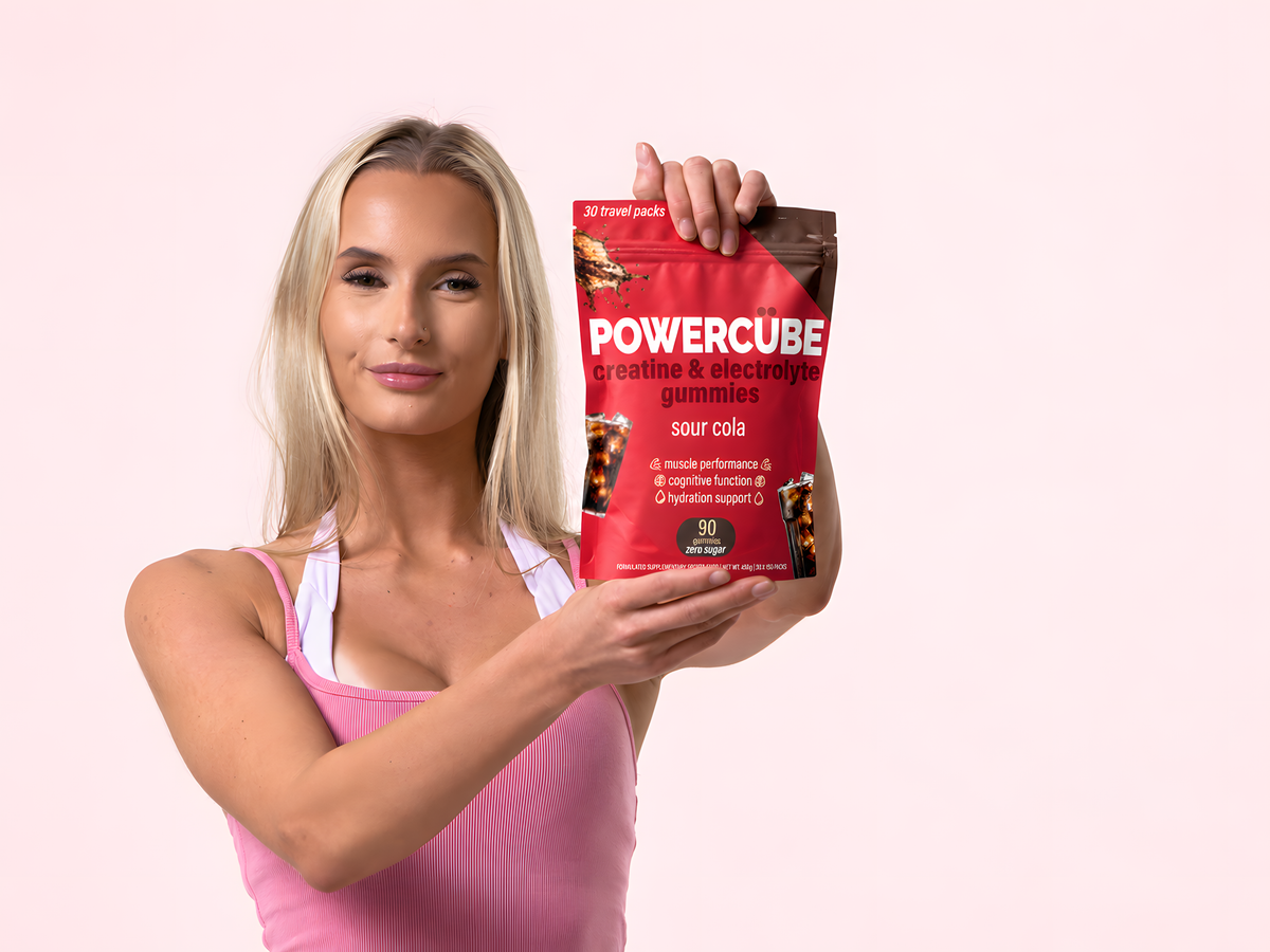 Woman in pink holding a PowerCUBE Sour Cola creatine and electrolyte gummies pouch.