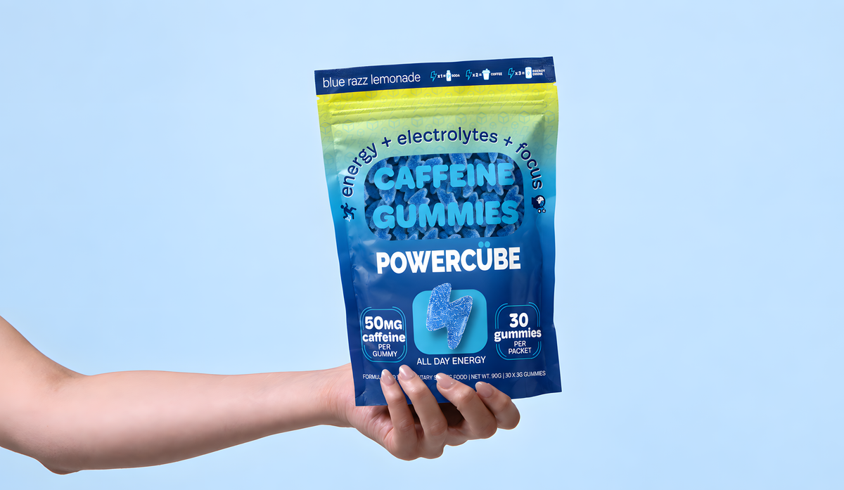 Hand holding a PowerCUBE Blue Razz Lemonade caffeine gummies pouch against a light blue background.