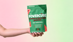 Hand holding a PowerCUBE Sour Watermelon creatine and electrolyte gummies pouch against a light pink and green background.
